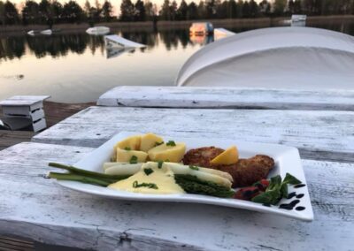 Schnitzel mit Spargel und Kartoffeln auf einem Teller mit Blick auf See bei Sonnenuntergang
