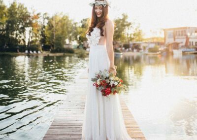 Braut mit Brautkleid steht mit Blumen in der Hand auf dem Steg mitten im Wasser