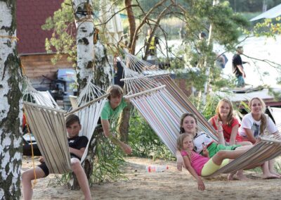 Kinder und Jugendliche liegen in einer Hängematte, die an Bäumen festgemacht ist