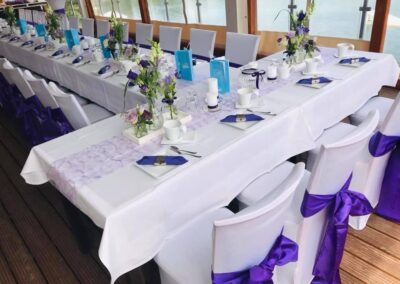 Eingedeckter Hochzeitstisch mit lila Schleifen an den Stuhlhussen und lila farbenen Akzenten auf dem Tisch