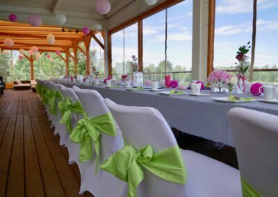 Langer Tisch hochzeitlich eingerichtet mit Hussen an den Stühlen und grünen Schleifen