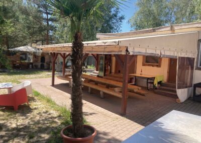 Hostel mit Vordach und Sitzbänken aus Holz neben einer Palme