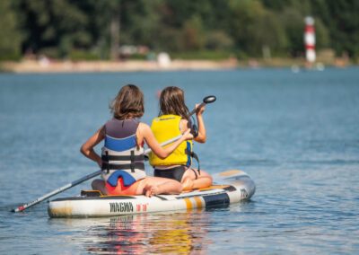 Zwei Mädchen sitzen auf einem Stand-Up-Paddle und paddeln in Richtung des weit entfernten Ufers