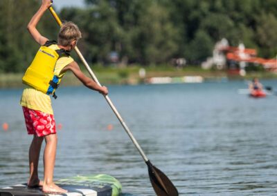 Junge paddelt mit einem Stand-Up-Paddle auf dem See in Richtung Ufer