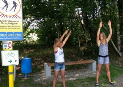 Zwei junge Mädchen üben die Sportbewegung Armkreisen inmitten im Grünen aus
